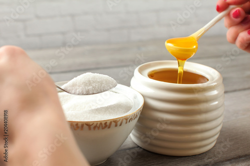 Canvastavla Detail on woman hand, one holding honey dipper with natural honey, other silver spoon with refined white sugar