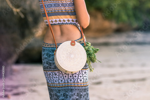 Woman hands with fashionable stylish rattan bag outside. Tropical island of Bali, Indonesia. Rattan and silk. photo