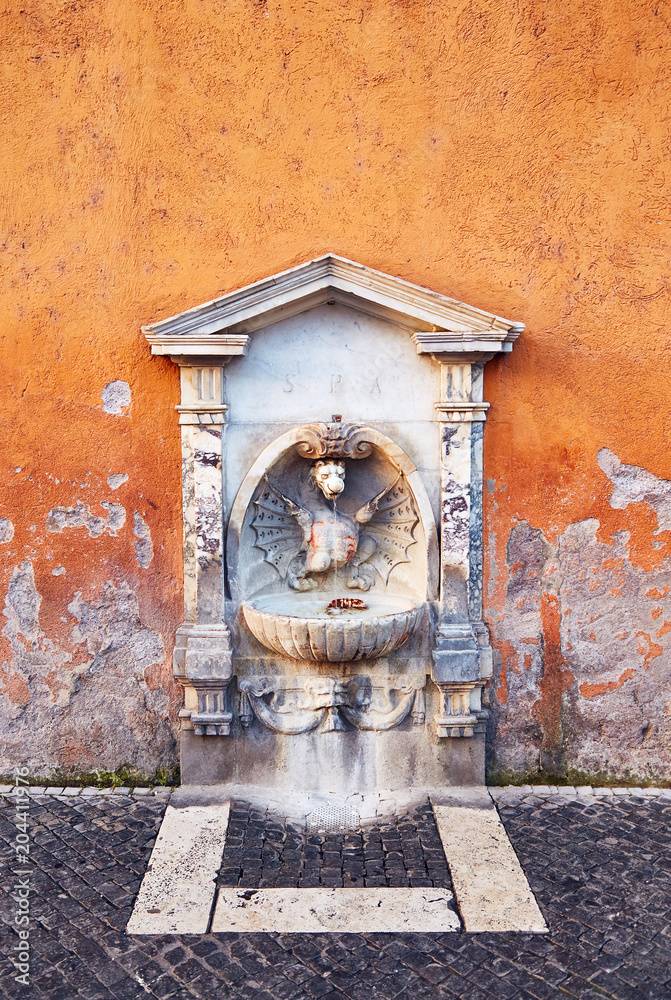 Small drinking fountain with sculpture and stone decor in shabby painted wall, Rome. Small drinking fountain with sculpture and stone decor in shabby painted wall, Rome.