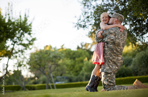 Male soldier hugging his young daughter in the back yard of their home.