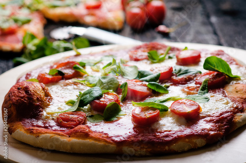 Italian food, cuisine. Margherita pizza on a black, wooden table with igredients like tomatoes, salad, cheese, mozzarella, basil. Delicious homemade food.  photo