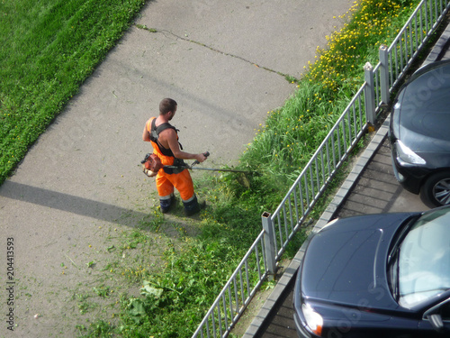 Man mows grass and dandelions near the Parking