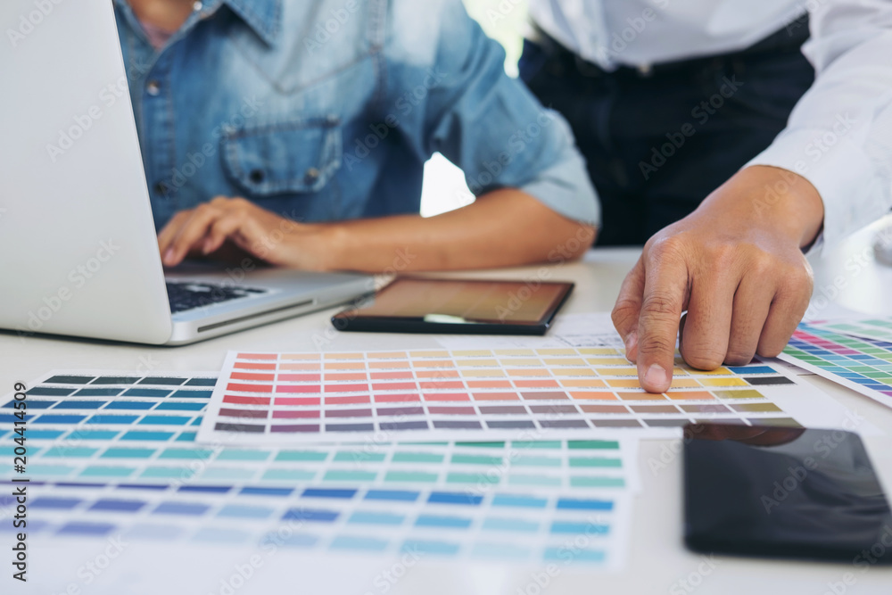 Two young interior design or graphic designer working on project of architecture drawing with work tools and color swatches, colour chart in digital tablet at workplace Two young interior design or graphic designer working on project of architecture drawing with work tools and color swatches, colour chart in digital tablet at workplace