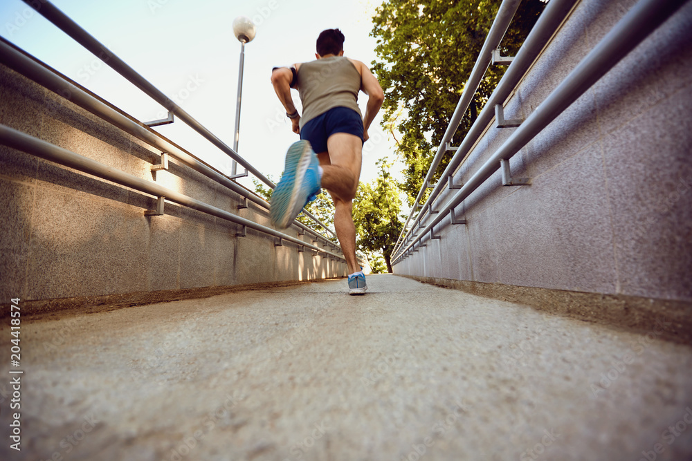 A male runner runs along the road to the park in the summer. A male runner runs along the road to the park in the summer.