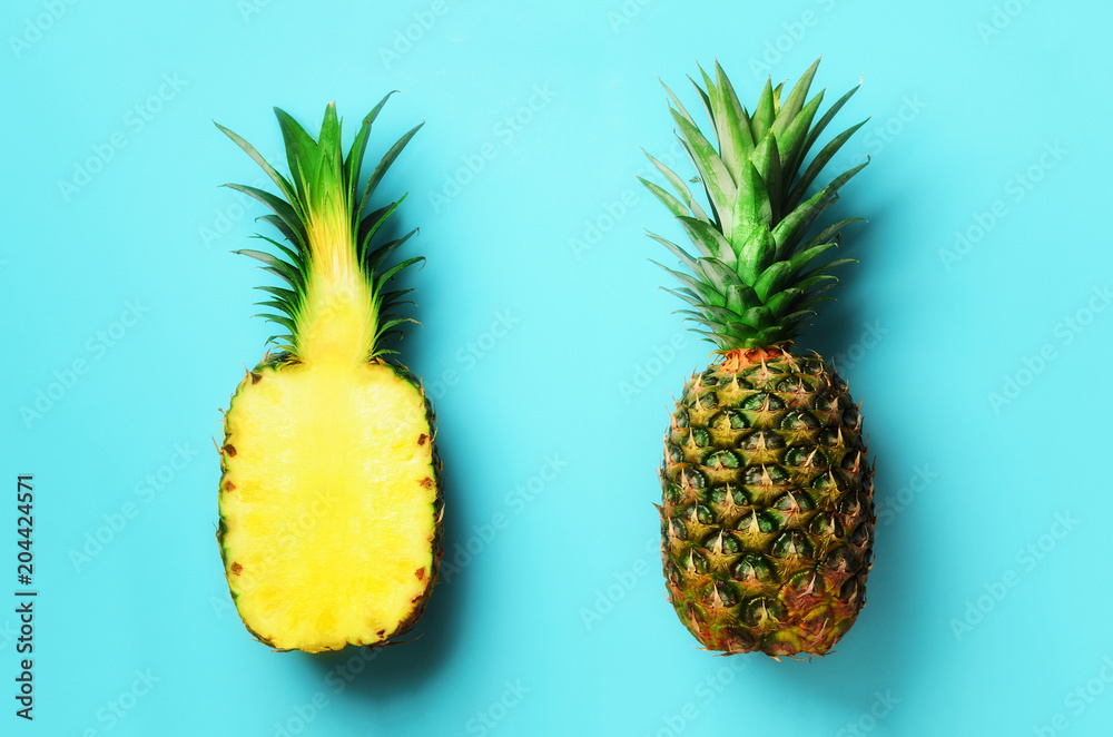 Fototapeta Cały ananas i połówka pokrajać owoc na błękitnym tle. Widok z góry. Skopiuj miejsce. Jasny wzór ananasa dla minimalistycznego stylu. Pop-art design, koncepcja kreatywna