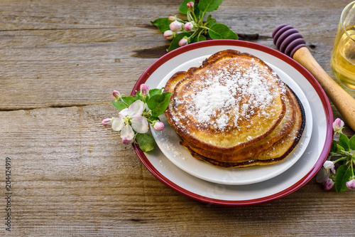 Sweet homemade pancakes with powdered sugar on a plate, decorated with flowers of an apple tree on a wooden background.