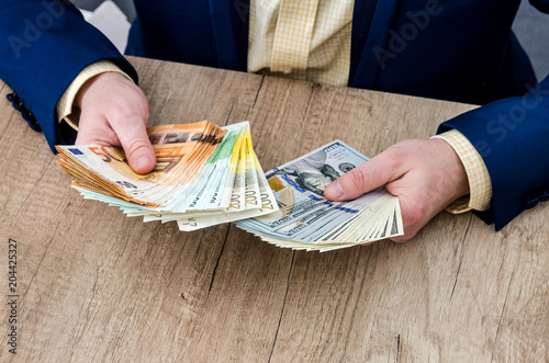 Wallpaper Mural Businessman counting dollar and euro banknotes behind wooden table Torontodigital.ca