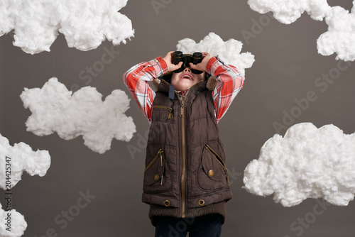 boy dressed as an airplane pilot stands between the clouds and looks through binoculars