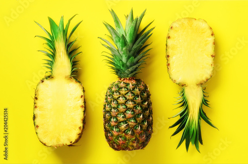 Half slice of fresh pineapple and whole fruit on yellow background. Top View. Copy Space. Bright pineapples pattern for minimal style. Pop art design, creative concept