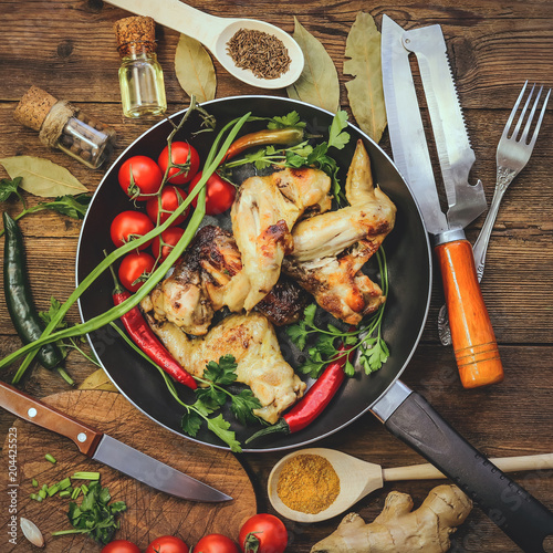 fried chicken wings in a frying pan with tomatoes. wooden background photo