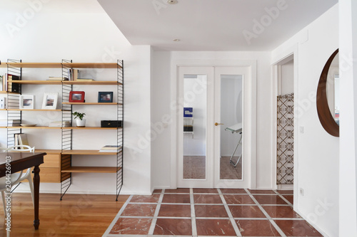 Hall with red and white marble floor next to the living room with a wood floor, wood table and wood shelves
