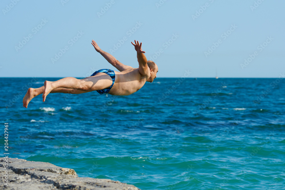 Young healthy man jumping into the sea from pier