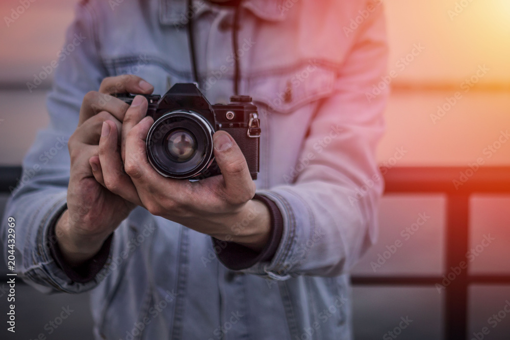 A man in a denim jacket with a vintage film camera at sunset