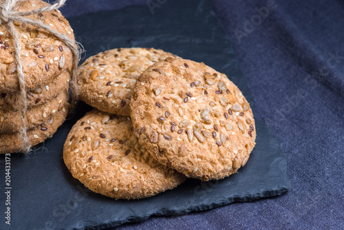 homemade oat cookies with sunflower seeds on shale board and dark blue textile background