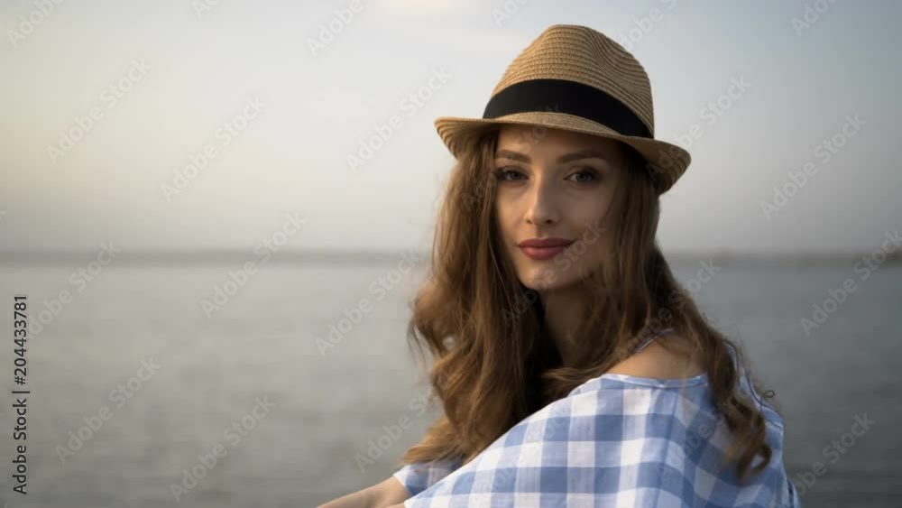 Close up. Attractive woman in hat and dress is sitting and looking at sunset Close up. Attractive woman in hat and dress is sitting and looking at sunset