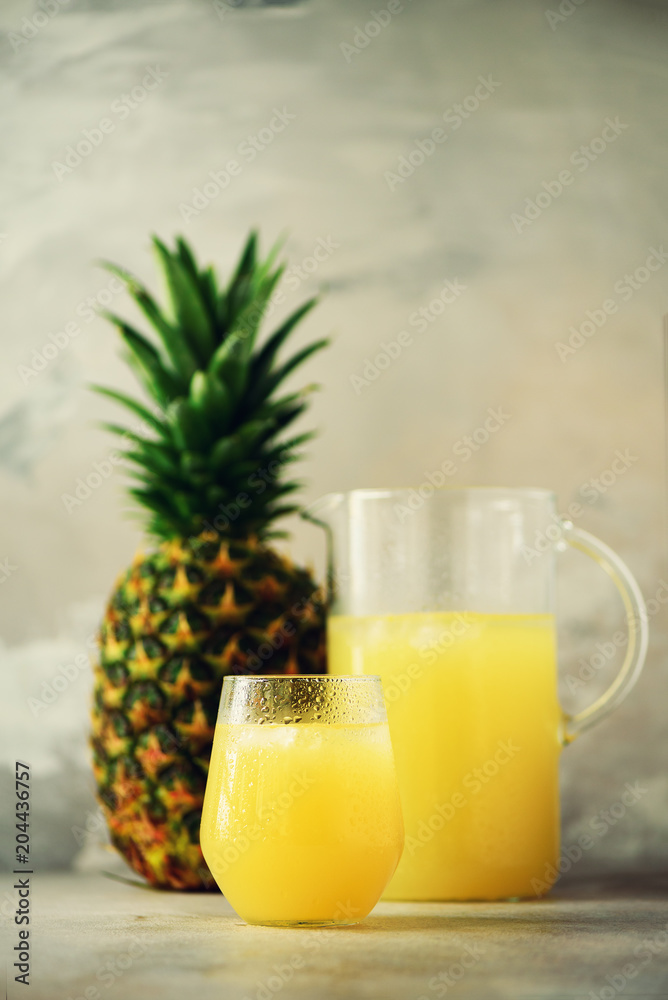 Pineapple juice in glassware and whole pineapple fruit on gray background. Copy space, sunlight effect. Summer, holiday concept. Raw, vegan, vegetarian, clean eating diet. Pineapple juice in glassware and whole pineapple fruit on gray background. Copy space, sunlight effect. Summer, holiday concept. Raw, vegan, vegetarian, clean eating diet.
