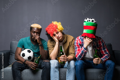 Fotografie Three friends fanatic football fans watching soccer game on television with beer