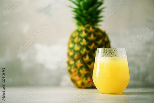 Glass of pineapple smoothie and whole fruit on gray background. Copy space. Summer, holiday concept. Raw, vegan, vegetarian, clean eating diet.