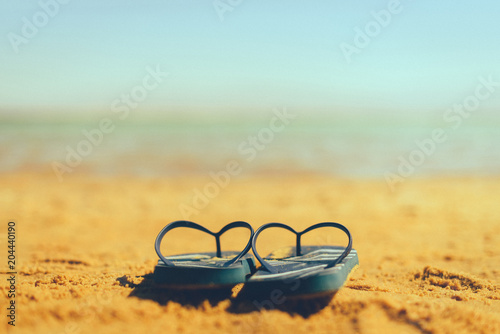 Navy flip flop on yellow sand beach with blue sea and sky background. Copy space. Summer, holiday and travel concept