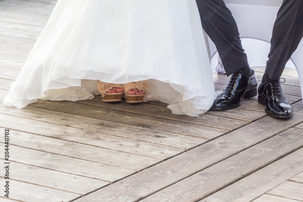 Braut Bräutigam sitzen bei Hochzeit und Trauung nebeneinander. Mann und  Frau tragen Luxus Hochzeitskleid, Anzug und Schuhe. Das Mädchen zeigt Füsse  mit Nagellack. Der schwarze Schuh ist poliert Stock Photo | Adobe