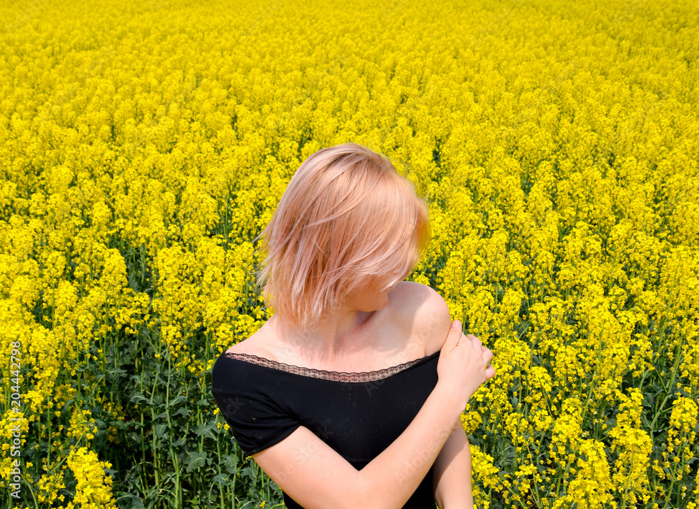 Fototapeta premium A girl in a black dress in a field of flowering rape.