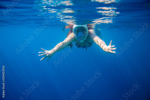 Snorkeling girl in full-face snorkeling mask undersea. Woman swimming