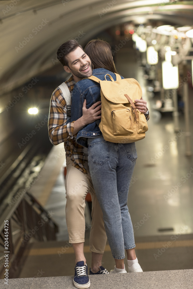 stylish male tourist with backpack hugging girlfriend at subway station
