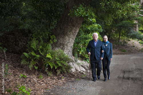木々が生い茂る道を歩く老夫婦。 © Monet