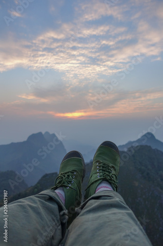trekking boots of traveller sitting on a high mountain at sunset