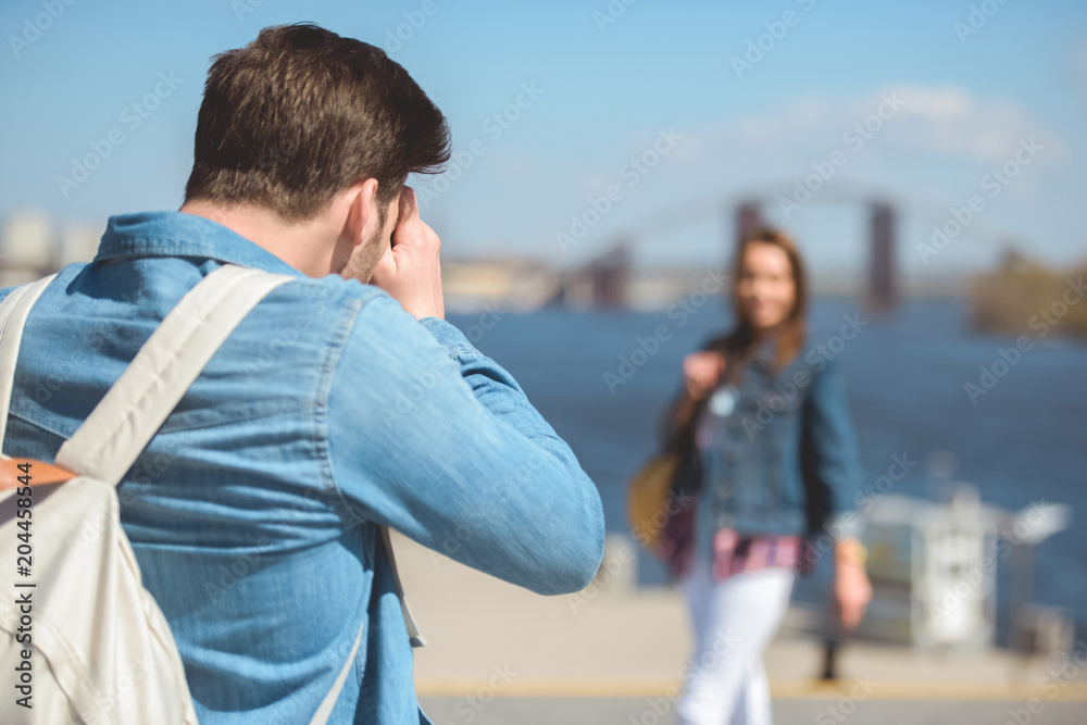 rear view of male traveler with backpack shooting girlfriend on camera rear view of male traveler with backpack shooting girlfriend on camera