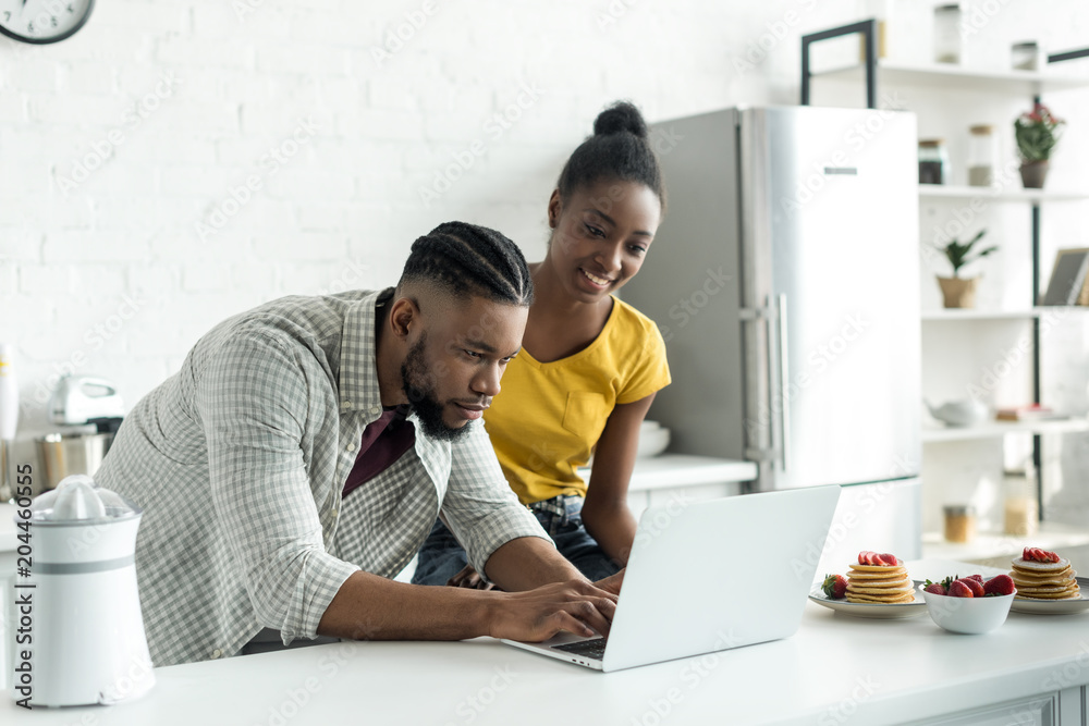 african american couple using laptop at kitchen african american couple using laptop at kitchen