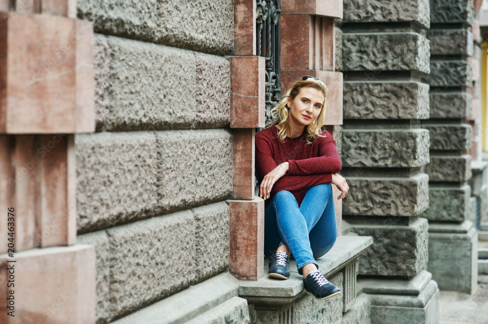 A young woman on a city street . Stylish lady in jeans and Burgundy sweater in the city . The concept of casual wear