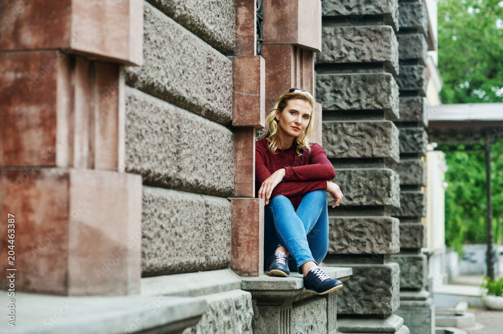 A young woman on a city street . Stylish lady in jeans and Burgundy sweater in the city . The concept of casual wear A young woman on a city street . Stylish lady in jeans and Burgundy sweater in the city . The concept of casual wear