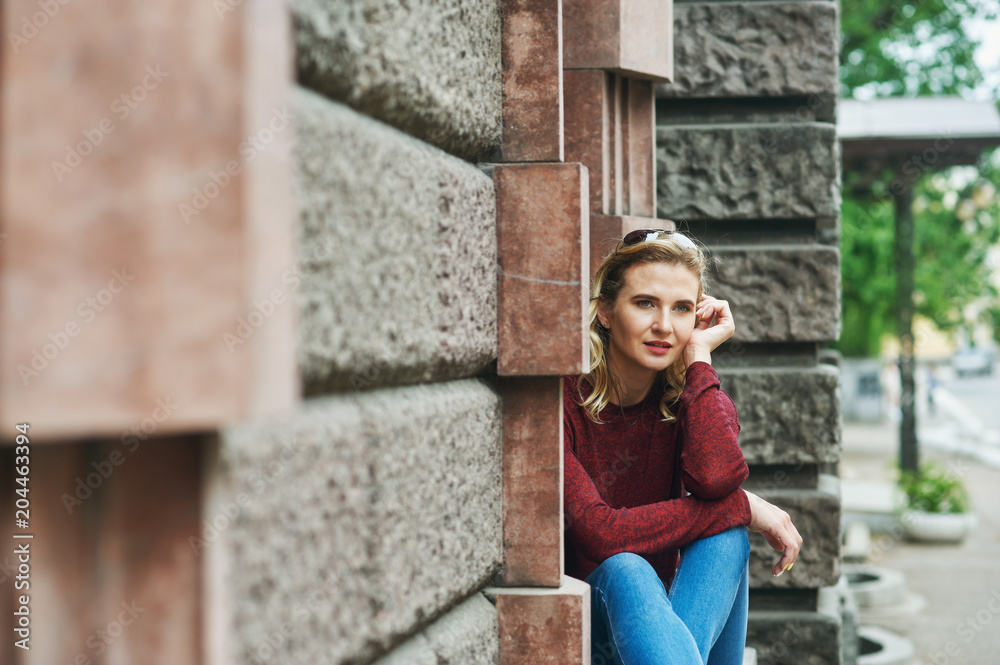 A young woman on a city street . Stylish lady in jeans and Burgundy sweater in the city . The concept of casual wear