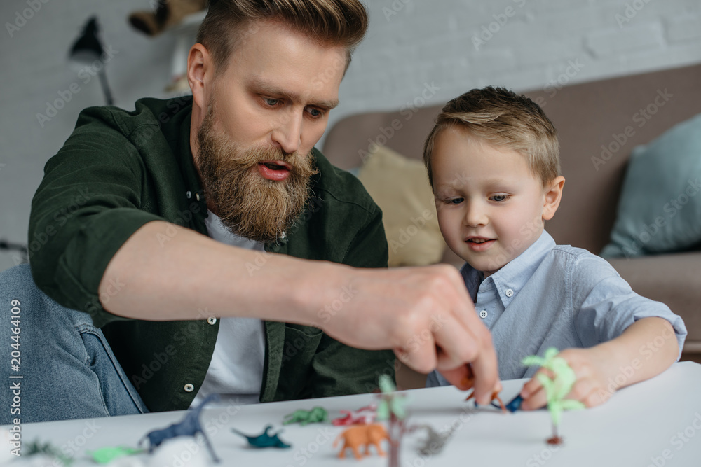 father and cute little son playing with various toy dinosaurs together at home father and cute little son playing with various toy dinosaurs together at home