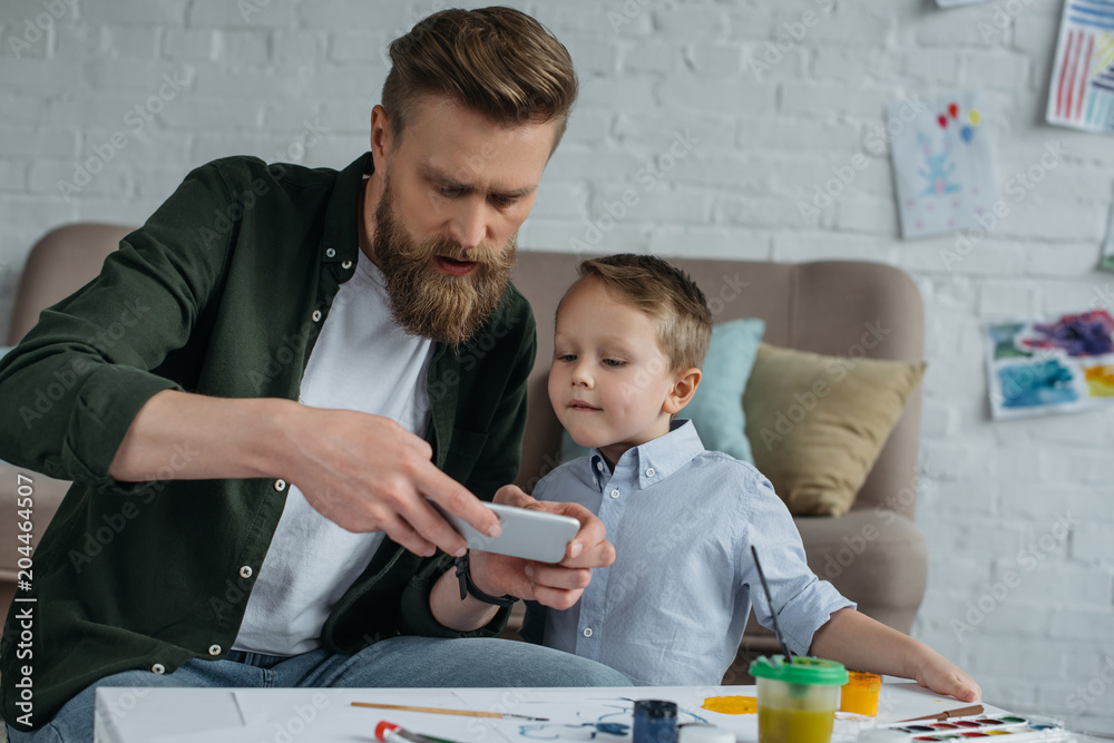 man taking photo of sons picture on smartphone at home man taking photo of sons picture on smartphone at home