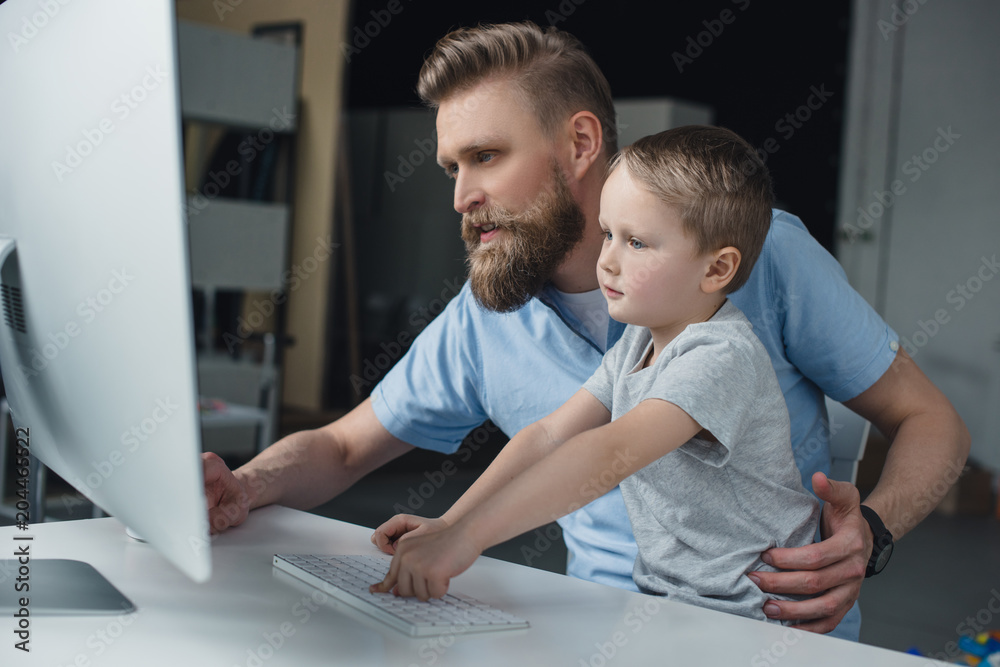 Obraz premium father and little son looking at computer screen while using computer at home