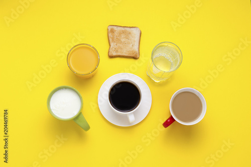 Healthy breakfast concept. Group of Drinks in Multicolored Cups, Black Coffee, Coffee with Milk, Yogurt, Just Water, Orange Juice and Toasts on a Yellow Background. Flat lay, top view