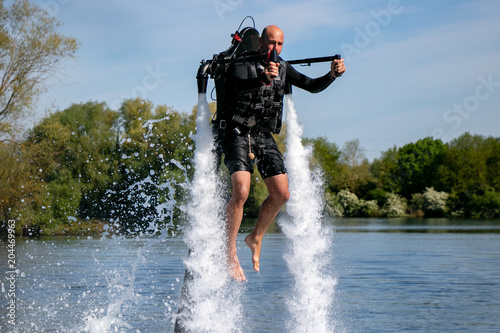 Thrillseeker, water sports lover, athlete strapped to Jet Lev, levitation hovers over lake with blue sky and trees photo