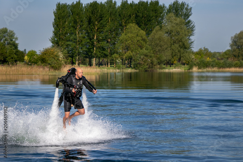 Thrillseeker, water sports lover, athlete strapped to Jet Lev, levitation hovers over lake with blue sky and trees