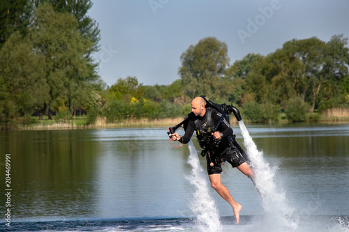 Thrillseeker, water sports lover, athlete strapped to Jet Lev, levitation hovers over lake with blue sky and trees photo
