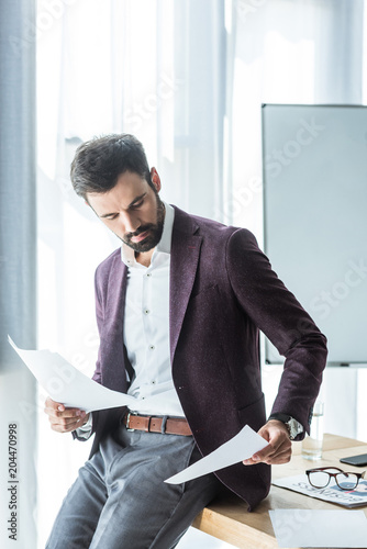 handsome young businessman doing paperwork while leaning back on desk at office