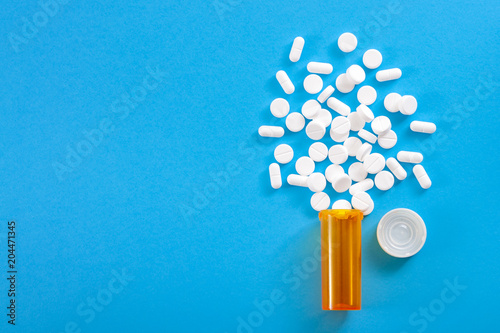 Medicine, opioid painkillers and prescription medicines concept with top view of orange prescription bottle of oxycodone and hydrocodone pills spilled on a blue background with copy space photo