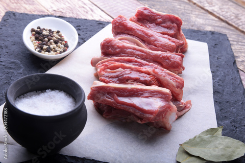 Raw fresh meat, uncooked lamb or beef ribs with pepper, garlic, salt and spices on dark stone background, Ready for cooking. copy space.