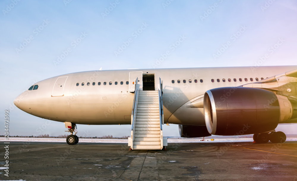 Wide body passenger airplane with a boarding stairs at the airport apron in the evening sun - obrazy, fototapety, plakaty 