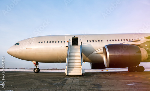 Wide body passenger airplane with a boarding stairs at the airport apron in the evening sun