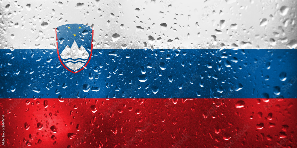 Texture of the Slovenia flag on the glass with drops of rain at dawn.
