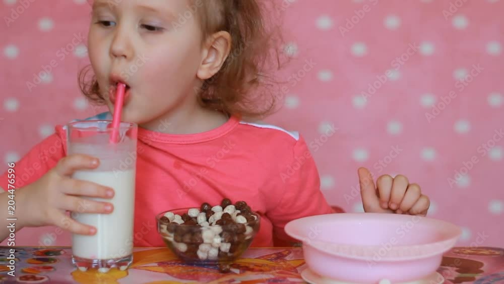 Girl child eats breakfast flakes and drinks a milk drink from a straw. Girl child eats breakfast flakes and drinks a milk drink from a straw.