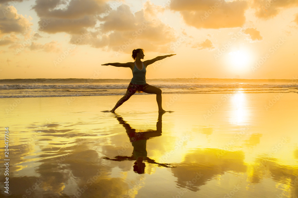 silhouette of young fit and healthy attractive woman practicing fitness and yoga in beautiful sunset beach in meditation and relaxation concept