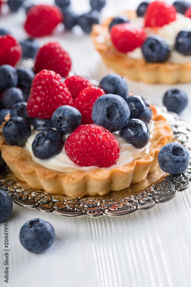 Dessert tarts with raspberries and blueberries on a wooden table.